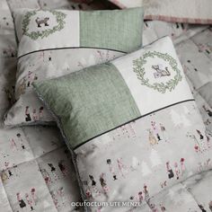 two pillows on top of a bed covered in white and green fabric with christmas decorations