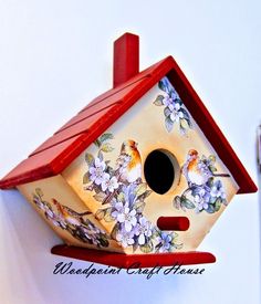 a bird house hanging from the side of a wall with flowers and birds painted on it