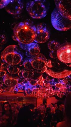 many disco balls hanging from the ceiling in a room with people sitting and standing around