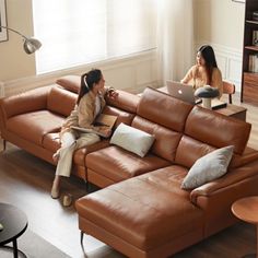 two women sitting on couches in a living room, one using a laptop computer