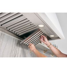 a woman is adjusting the light on an exhaust fan above her kitchen stove top hood