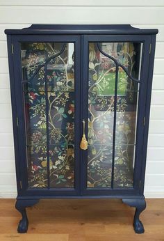 an old china cabinet with glass doors and floral wallpaper on the door, painted in dark blue