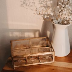 a vase with some flowers in it next to a glass box on a wooden table