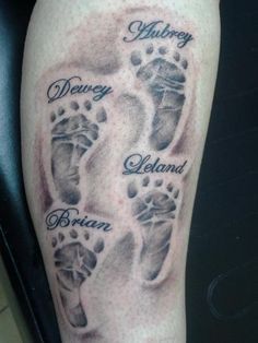 a tattoo on the leg of a person with two baby feet and name written in black ink