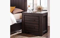 a night stand with two drawers and a bed in the background