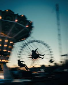 two people are flying through the air on a ferris wheel at night with lights in the background