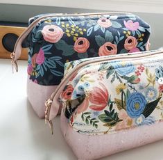 two small floral bags sitting on top of a white counter next to each other, one with pink and blue flowers