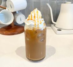 a drink with whipped cream and caramel on top sits on a counter next to a coffee maker