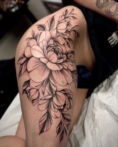 a woman's thigh with flowers on it in black and grey ink, sitting on a bed