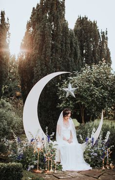 a bride sitting on the moon surrounded by flowers and greenery in front of trees