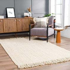 a living room with a rug, chair and sideboard on the floor in front of a window