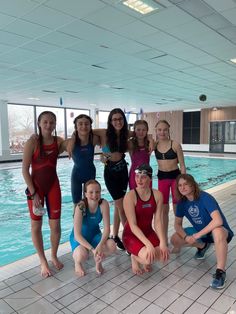 a group of women standing next to each other in front of an indoor swimming pool