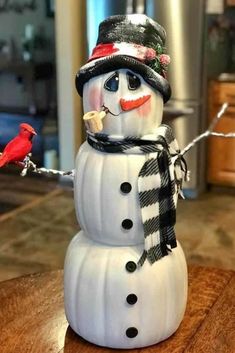 a snowman with a hat, scarf and bird on it's nose sitting on a table