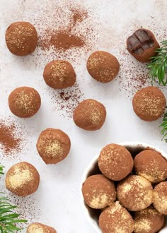 a white bowl filled with chocolate truffles and sprinkles next to pine branches