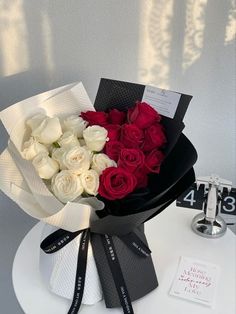 a bouquet of white and red roses sitting on top of a table next to a clock