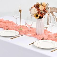 the table is set with white plates and gold place settings, along with pink ruffle runner