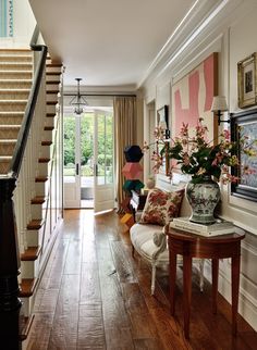 a living room filled with furniture and flowers on top of a hard wood floor next to a stair case