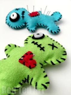 two green and one blue stuffed animals with pins in their ears on a white surface