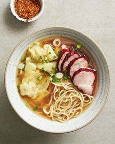 a bowl of soup with meat, noodles and garnishes on the side