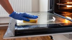 a person in blue gloves is cleaning an oven with a sponge and soap on it