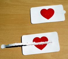 two white tags with red hearts cut out of them sitting on a table next to each other