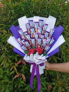 someone is holding a bouquet of chocolates with roses in the front and purple ribbon around it