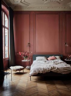 a bedroom with red walls and wooden floors, an upholstered bed in the middle