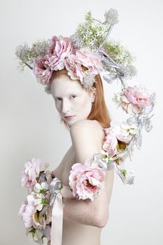 a woman with red hair and flowers on her head is posing in front of a white background