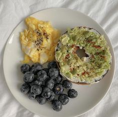 a bagel, blueberries and scrambled eggs are on a plate with white linen