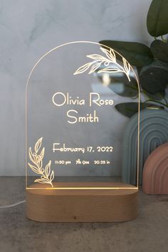 an illuminated glass plaque with the name and date on it next to a potted plant