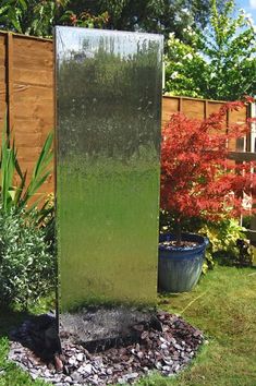 a large metal water fountain in the middle of a yard with trees and bushes behind it