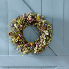 a wreath hanging on the side of a blue barn door with flowers in front of it