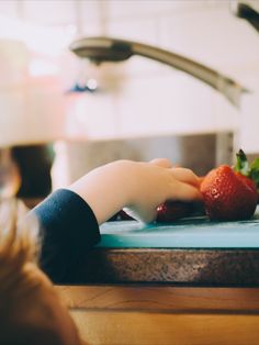 a little boy is cutting up some strawberries on a blue counter with a faucet in the background