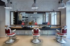 two red chairs sitting in front of a mirror with lights hanging from it's sides