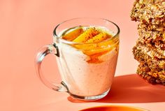 two cookies and a glass of milk on a pink background with an orange plate next to it