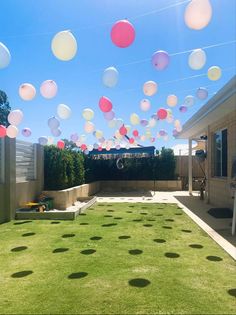 some balloons are flying in the air over a yard with green grass and small bushes