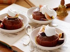 three small white bowls filled with desserts on top of a wooden table next to an open book