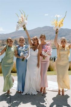 four women in dresses are holding flowers and posing for the camera with their hands up