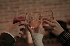 three people toasting with wine glasses in front of a brick wall and holding each other's hands