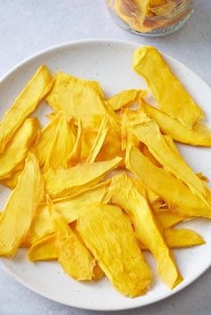 a white plate topped with cut up pieces of yellow fruit next to a jar of orange juice