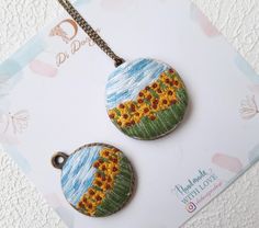 two sunflowers are painted on the back of small pendants, one is hanging from a chain