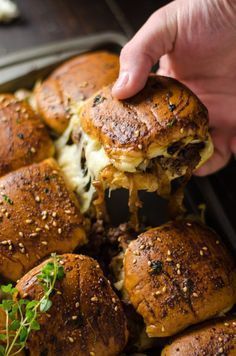 someone is picking up some sliders out of the pan with cheese and herbs on them