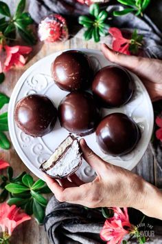 a person holding a plate with some chocolates on it and flowers in the background