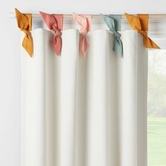 a window with white curtains and colorful bows on the valance, in front of a green field