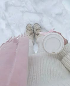 a person holding a white cup in the snow with their feet up and legs down