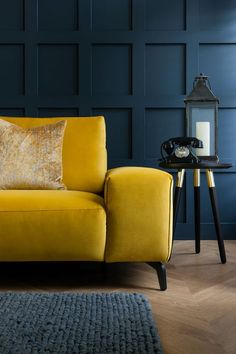 a yellow couch sitting on top of a wooden floor next to a table with a lamp