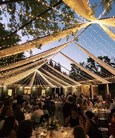 an outdoor tent with string lights and people sitting at tables under the canopy in front of it