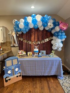 a blue and white table topped with balloons next to a wooden wall filled with decorations