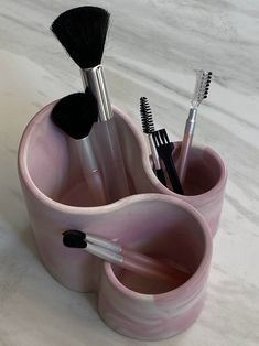 three makeup brushes in a pink cup on a marble counter top with the lid open