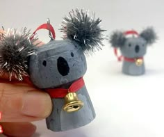 a hand is holding a tiny toy koala bear with silver hair and bells on its head